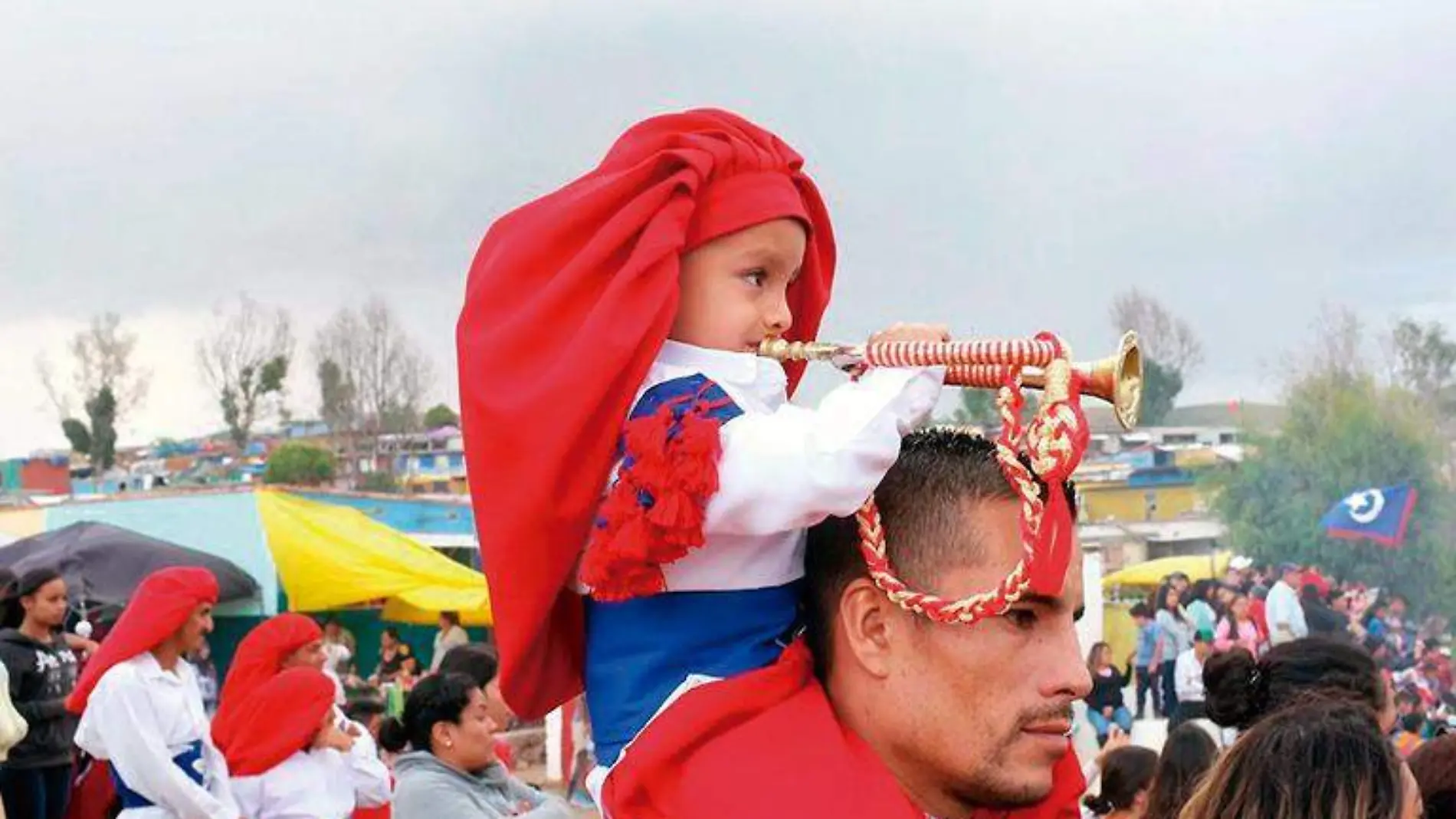 Niño toca una corneta sobre los hombros de su padre, durante la celebración de las Morismas de Bracho